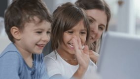 Mother and two preschool children using laptop computer for online communication, laughing and greeting someone they see on the screen