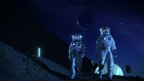 Two Astronauts in Space Suits Exploring Newly Discovered Planet. In the Background Space Base with Habitable Dome, in the Sky Outer Planets are seen. Futuristic Concept on Space Colonization.