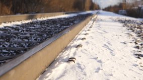Light snow flakes fly over rail tracks driven by breeze, closeup shot, low camera position with perspective. One railway line at city outskirts, winter season time, snow lie beside steel rail