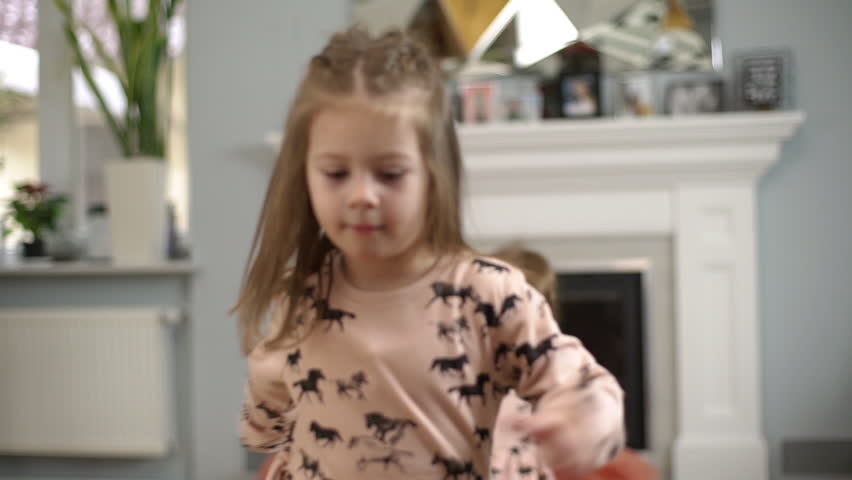 Two little joyful girls wearing dresses having fun, dancing and playing around at home in children room in slow motion