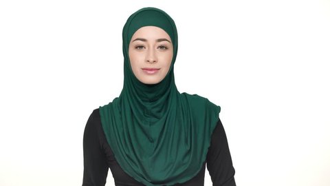 Portrait of young religious woman in traditional headscarf showing index finger on camera meaning hey you, over white background. Concept of emotions
