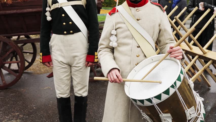 Close-up of military drummer in uniform of Napoleonic Wars knocks drumsticks with drum next to standing soldier, slow motion