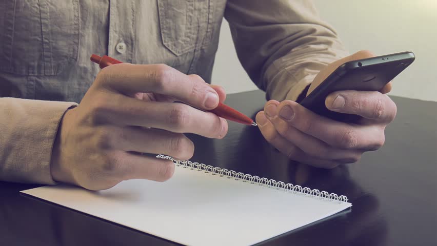 Hands close-up holding a phone Businessman at work with mobile phone in office. Scrolls application on your mobile phone. Man works by mobile, search on Internet information, makes notes in notepad
