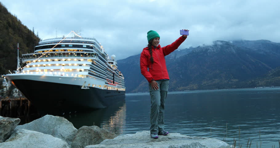 Tourist on Alaska cruise ship taking selfie photo in front of cruise ship in Skagway, Alaska, USA. Woman tourist taking picture using smart phone at night on travel vacation