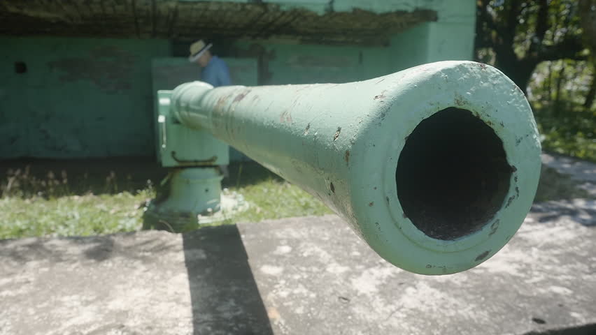 A medium shot of old metal cannon with a person examining it
