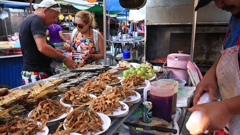 KOH PHANGAN, THAILAND - FEBRUARY 21, 2018 : Street trade food : Thai man cooking and sells sea fish on the night market in island Koh Phangan, Thailand