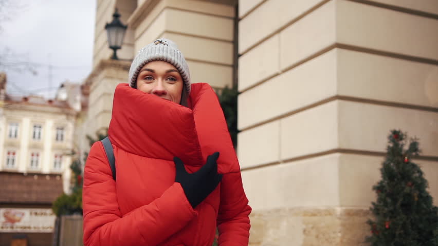 Beautiful woman in red winter jacket walks along the street covered with snow in a beautiful old European city