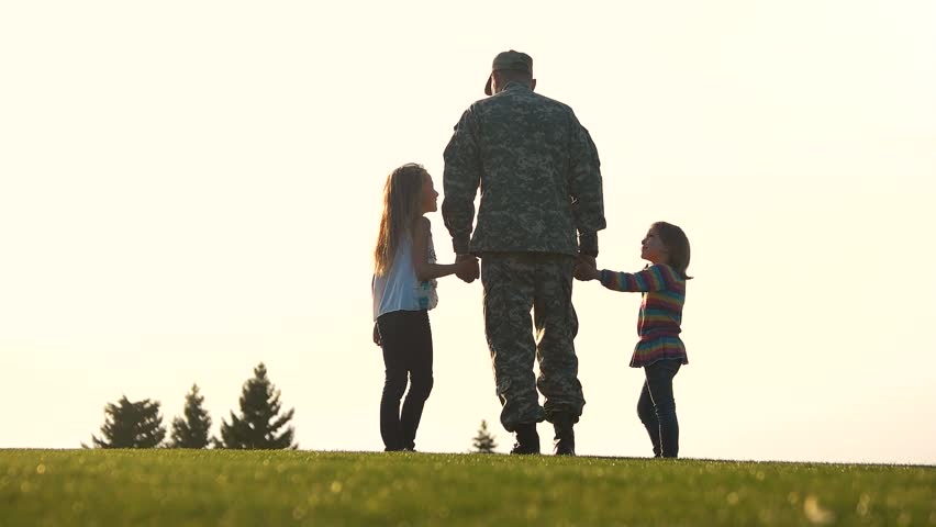 Back view soldier in uniform walk with daughters. Military man in camoubackgrounde walking holding hands of his little daughters.