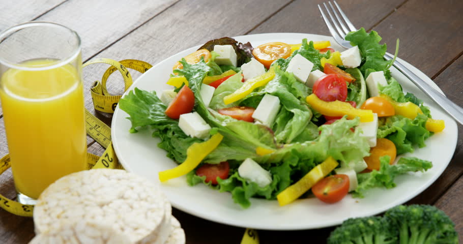 Vegetable salad with glass of juice, granola bar and measurement tape on wooden table