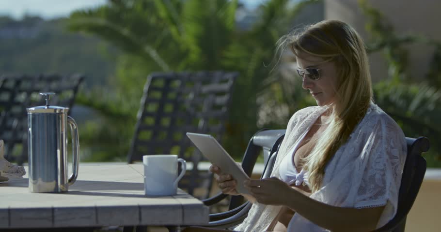 woman sitting with coffee and tablet at tropical villa