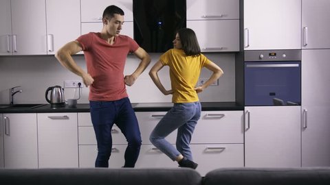 Young creative hipster couple dancing together in the kitchen at home. Fancy funny young people being silly and enjoying together celebrating after moving to their new house. Newlyweds in new home.