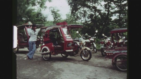 TAGAYTAY CITY, PHILIPPINES, APRIL 1978. A Rickshaw Driver Waiting For Customers, Posing In Front Of Numerous Red Tricycle Rickshaws, Smiles And Looks At The Camera.