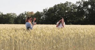 France, Provence, Two beautiful young girls are shooting photo in the field of wheat at sunset, happy girl with long hair, green trees on background