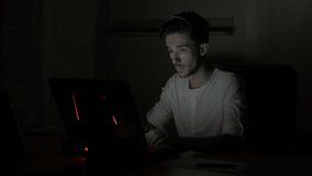 Young attractive student male video chatting and waving at web camera in a dark room at home