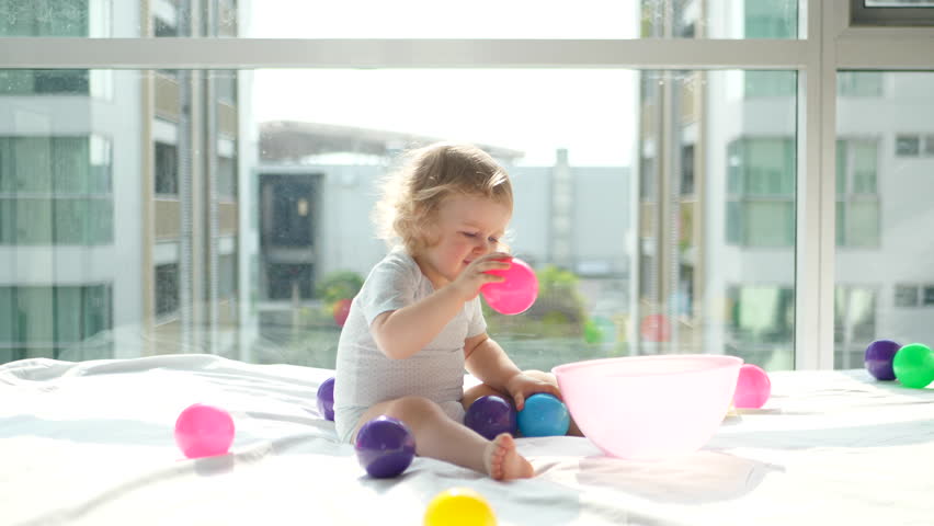 Baby plays with colorful balls on the bed. 4K UHD.