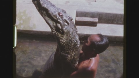 BANGKOK, THAILAND, JANUARY 1984. Two Shot Sequence Of An Older Animal Trainer, Holding Up And Hugging An Alligator While Waving To The Audience At The Samutprakarn Crocodile Farm Show.