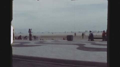 RIO DE JANEIRO, BRAZIL, MARCH 1976. Three Shot Sequence. Copacabana Beach Filmed Out Of The Window Of A Driving Car. Numerous VW Beetle Cars Parked At The Beach.
