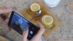 Close-up of woman hand with phone making photo slices of lemon in jar.