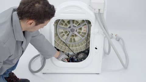 A repairman is fixing the back of the washing machine. He needs to find out where the problem is.