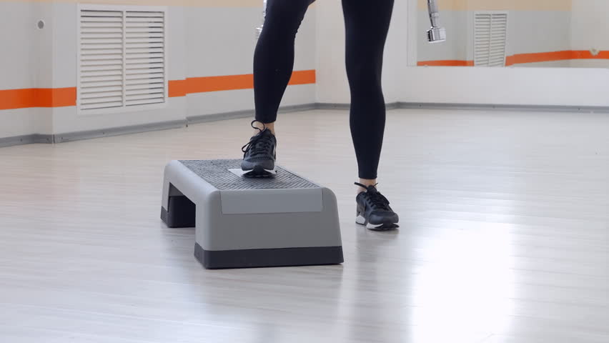 Trained woman performing squats with dumbbells on step platform