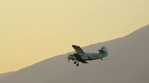 A crop duster applies chemicals to a field at sunset