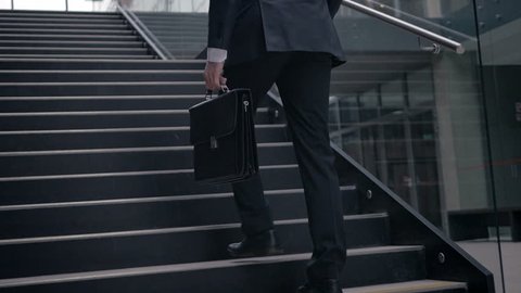 Slow motion of businessman climbing up the stairs in the office building. Confident man having a successful career in business.