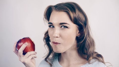 Seductive attractive woman in gray biting a green juicy apple and chewing it. She is looking at you. Locked down real time close up shot