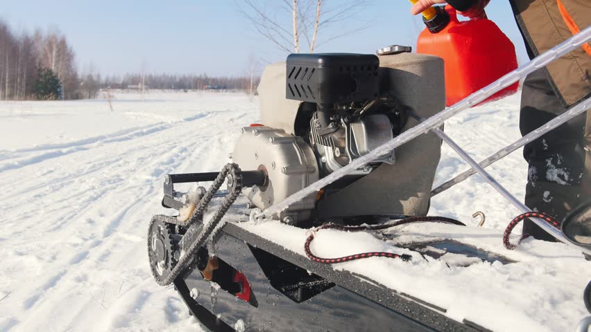 Man pours fuel into the gas tank of a mini snowmobile on a winter snowy road