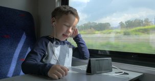 Child having a video call on smart phone in train, he using hands free set to talk