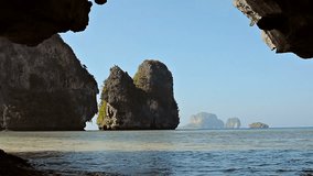 Video FullHD (1920x1080) - View of enormous rocks. towering over the tropical sea. taken from a sheltered position inside the mouth of a natural cave.