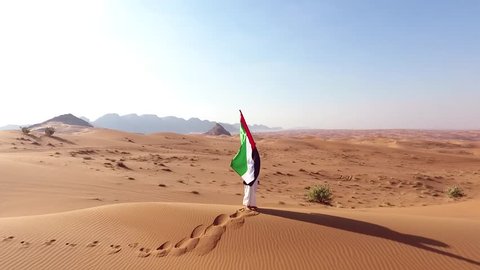arab emirati man holding UAE flag and walk in the Dubai Desert