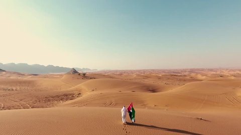 Proud arabian Emirati man holding a UAE flag, walking in the desert 