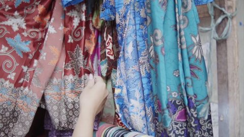 Stand of the colorful embroidered with threads and stamp print clothes in different colours at the traditional etnic asian market. Womans hand trying the quality of the textile material