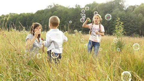 Happy family playing in nature. Mom and children are blowing bubbles. A girl and a boy are playing with her mother. Camping with the family. Glade near the forest. The sun is shining and it's raining.