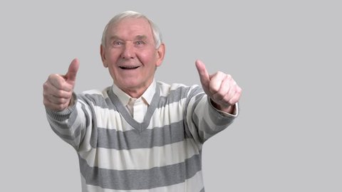 Happy grandfather with two thumbs up. Cheerful eldery man giving thumbs up sign on grey background. Gesture of success and happiness.