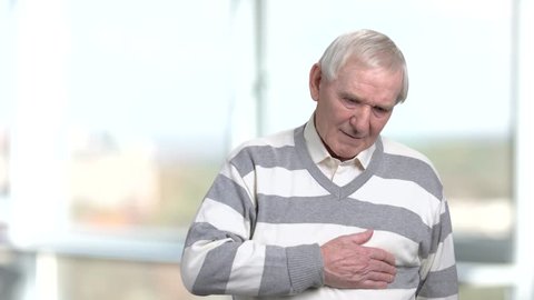 Unhappy senior massaging his chest. Older man holds his chest as he suffers from a heart attack, blurred background. Symptoms of heart problems.