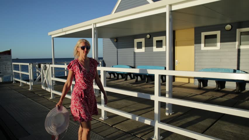 Carefree blonde woman enjoys the sunset light on famous Busselton wooden jetty in Busselton, Western Australia. Australian travel freedom. Female tourist in iconic place.