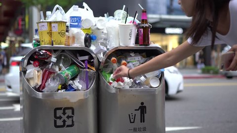 Taipei, Taiwan-13 August, 2017: 4K Trash spilling out of overfilled trash can on city street Taipei. Asian woman walking and throws garbage in dustbin on road. Bottles, cans and other trash litter-Dan