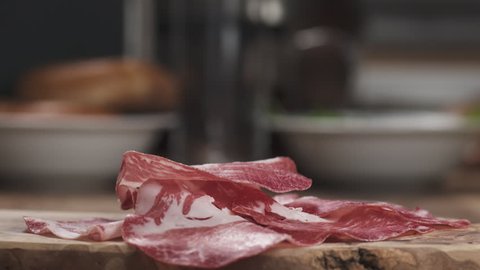 Slow motion of Italian coppa ham falling on wood board closeup