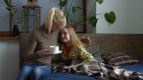 Attenitive mother giving her ill cute daughter a cup of hot tea. Sick little girl in pajamas with high fever lying in bed, coughing and drinking hot tea. Lovely ill child taking a medicine in the bed.