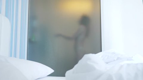 4k, slow motion. unrecognizable girl takes a shower. someone looks at it through the transparent wall between the bedroom and the bathroom. The woman behind the blurred glass. Woman in the bathroom.