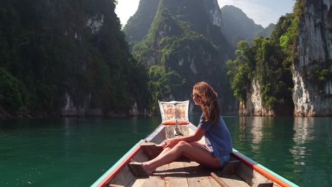 Wonder travel woman exploring wild nature of Khao Sok national park. Sitting in wood long tail boat on tropical limestone cliffs background. Lifestyle image. Island lagoon.