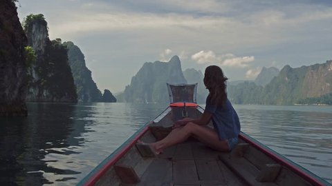 Lifestyle video of pretty travel woman sitting in wood long tail boat on tropical limestone cliffs . Explore and vacation concept. Khao Sok lake, Thailand.