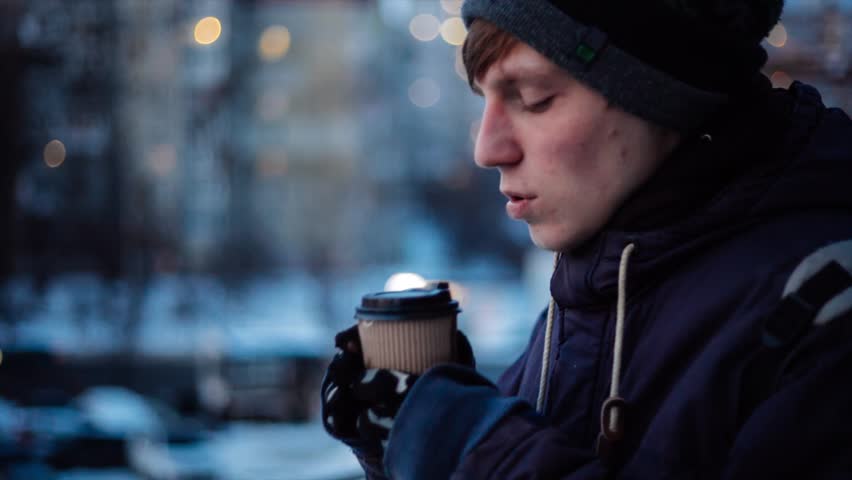 Young man drinking coffee and having cold while waiting someone outside on winter