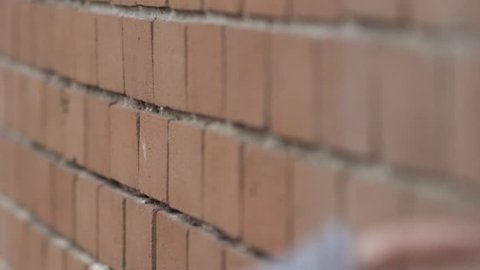 Hand of girl rubbing down brick wall in slow motion