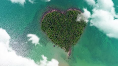 AERIAL. Camera moving trought clouds to heart shape island in Thailand.