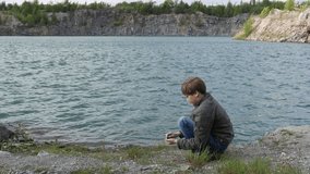 Happy caucasian teen boy throwing stones into the water of the lake. Ecology and environment, fresh air, clean water, Holiday.
