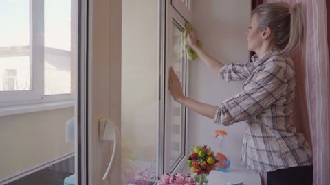 people, housework and housekeeping concept - woman cleaning the window with rag