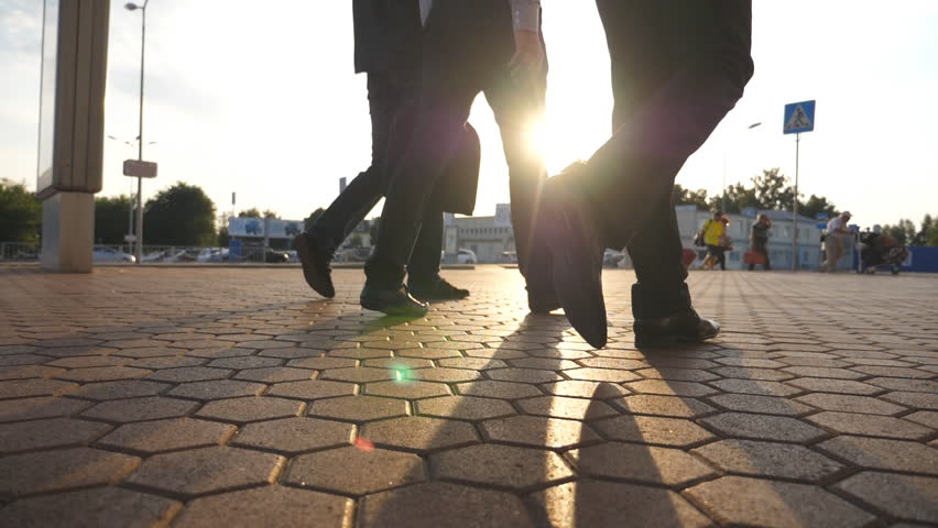 Feet of three businessmen walking near airport with sun flare at background. Business men go to terminal together. Confident guys being on his way to work trip. Colleagues going outdoor. Slow motion Royalty-Free Stock Footage #1007928586