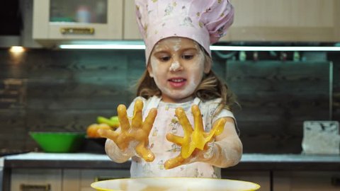 Pretty kid having fun in the kitchen and mixing pastry batter with hands.